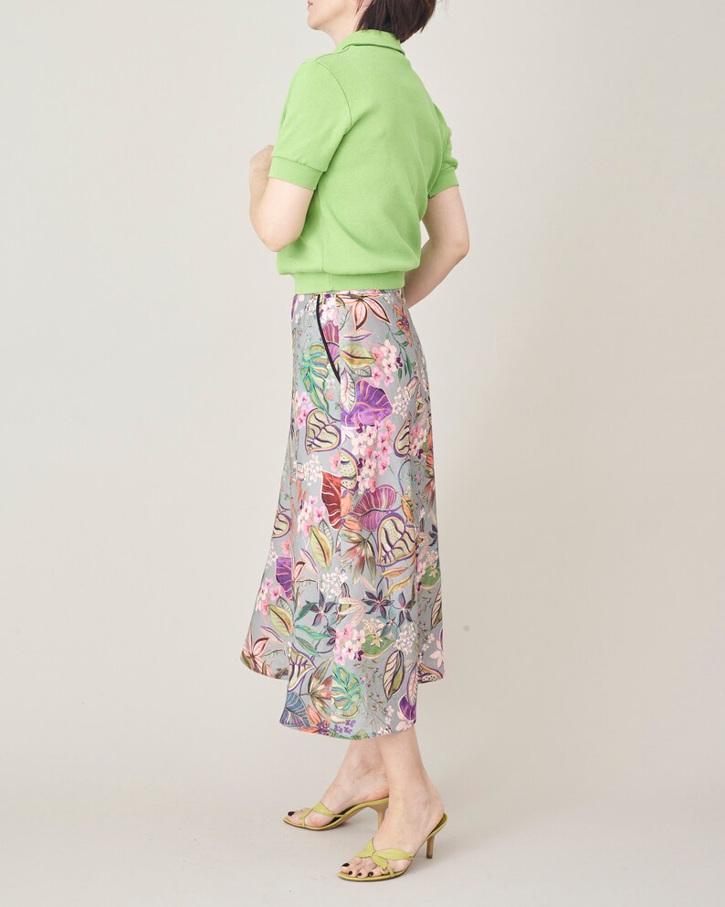 Person wearing a green polo shirt and floral skirt on a plain background