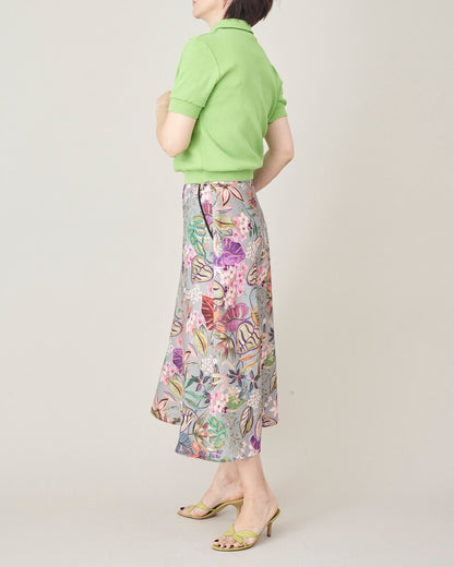Person wearing a green polo shirt and floral skirt on a plain background