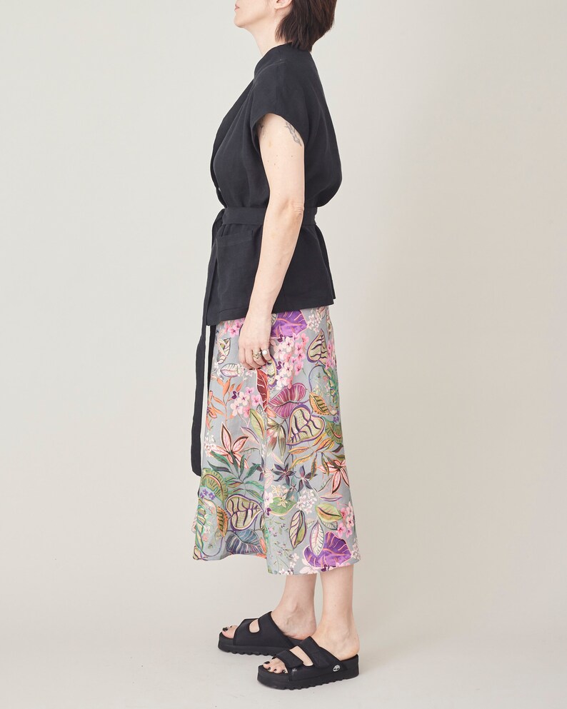 Person wearing a black top and colorful floral skirt on a plain background