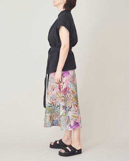 Person wearing a black top and colorful floral skirt on a plain background
