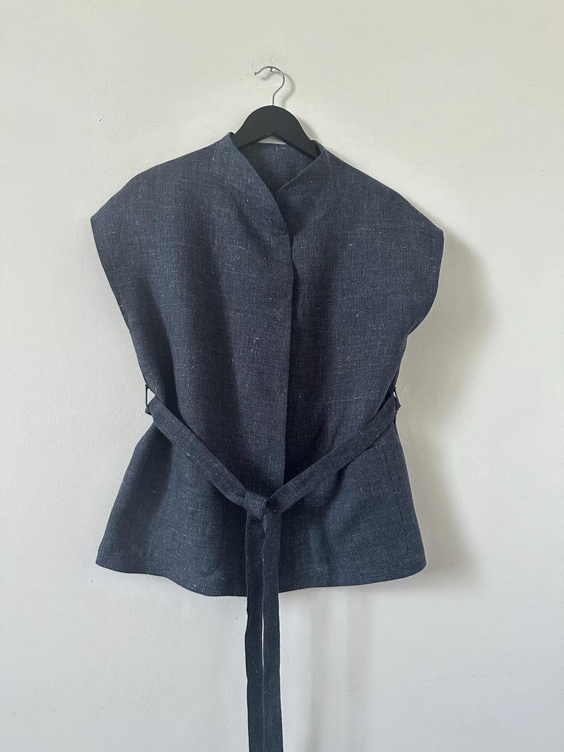 Blue sleeveless top with a belt on a hanger against a white background