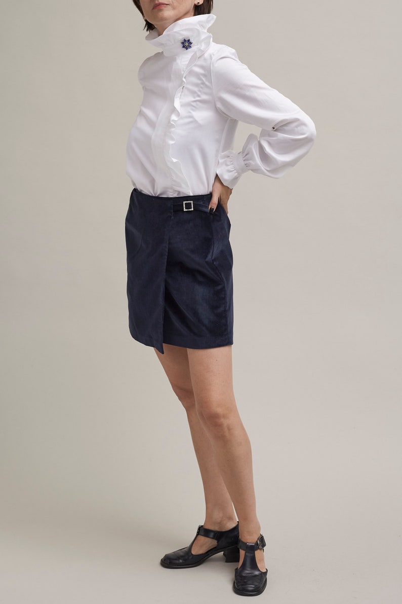 Person wearing a white blouse and navy skirt on a plain background