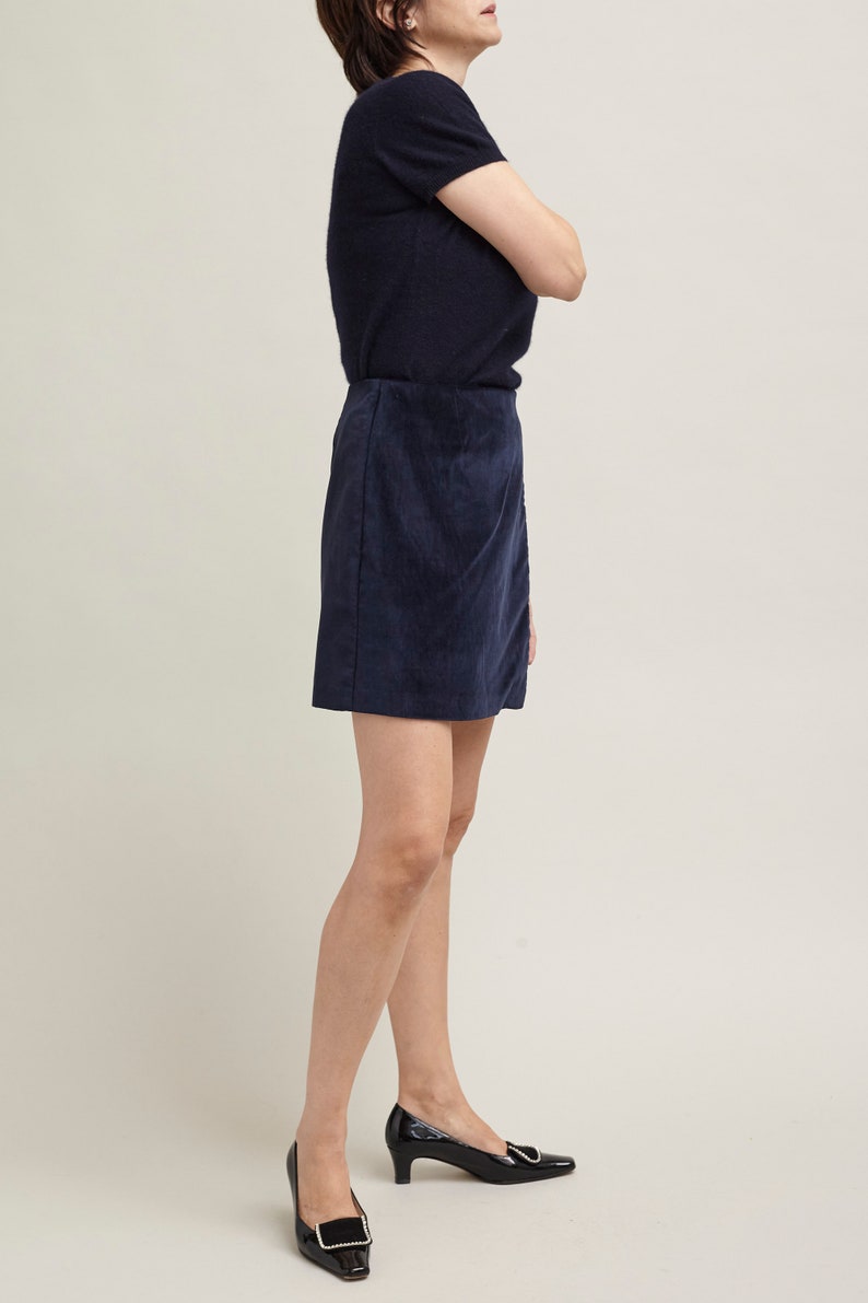 Person wearing a navy blue top and skirt with black shoes on a plain background