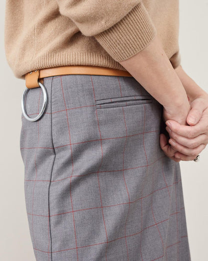 Person wearing a beige sweater and gray checkered skirt with a belt on a neutral background