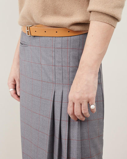Person wearing a beige sweater, brown belt, and gray plaid skirt on a plain background