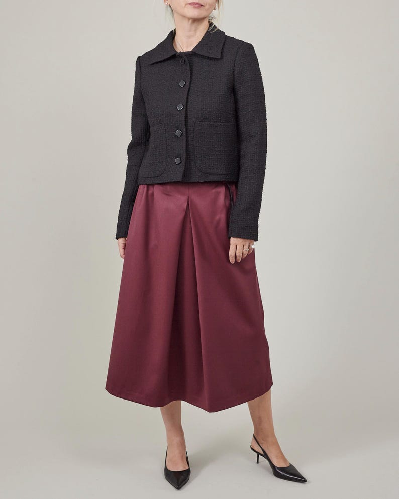 Person wearing a dark jacket and maroon skirt on a plain background