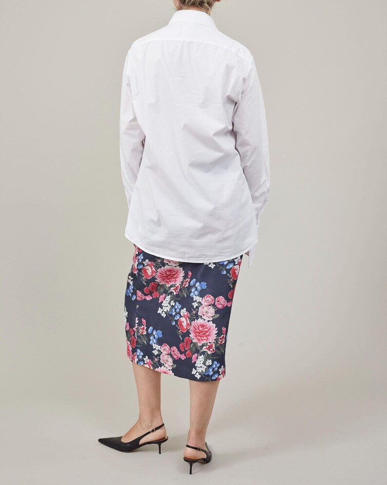 Person wearing a white shirt and floral skirt on a plain background