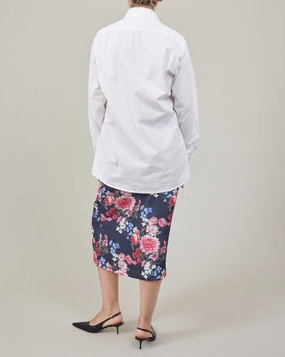 Person wearing a white shirt and floral skirt on a plain background