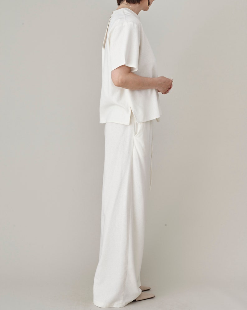 Side profile view of women's natural ivory raw silk wide-leg trousers with pocket details, styled as a coordinated premium loungewear set by Fine Thee