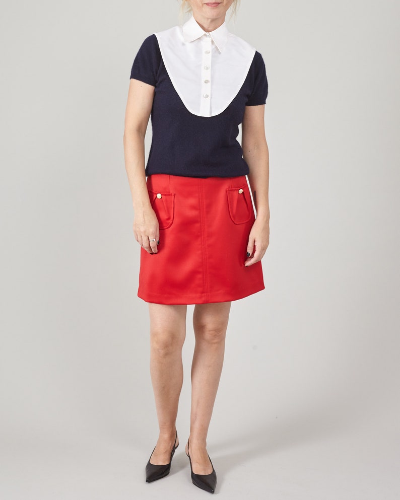 Person wearing a navy top with white collar and red skirt in studio