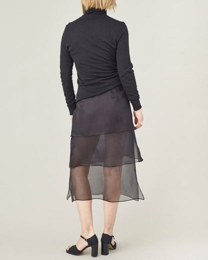 Person wearing a black long-sleeve top and sheer black skirt on a white background