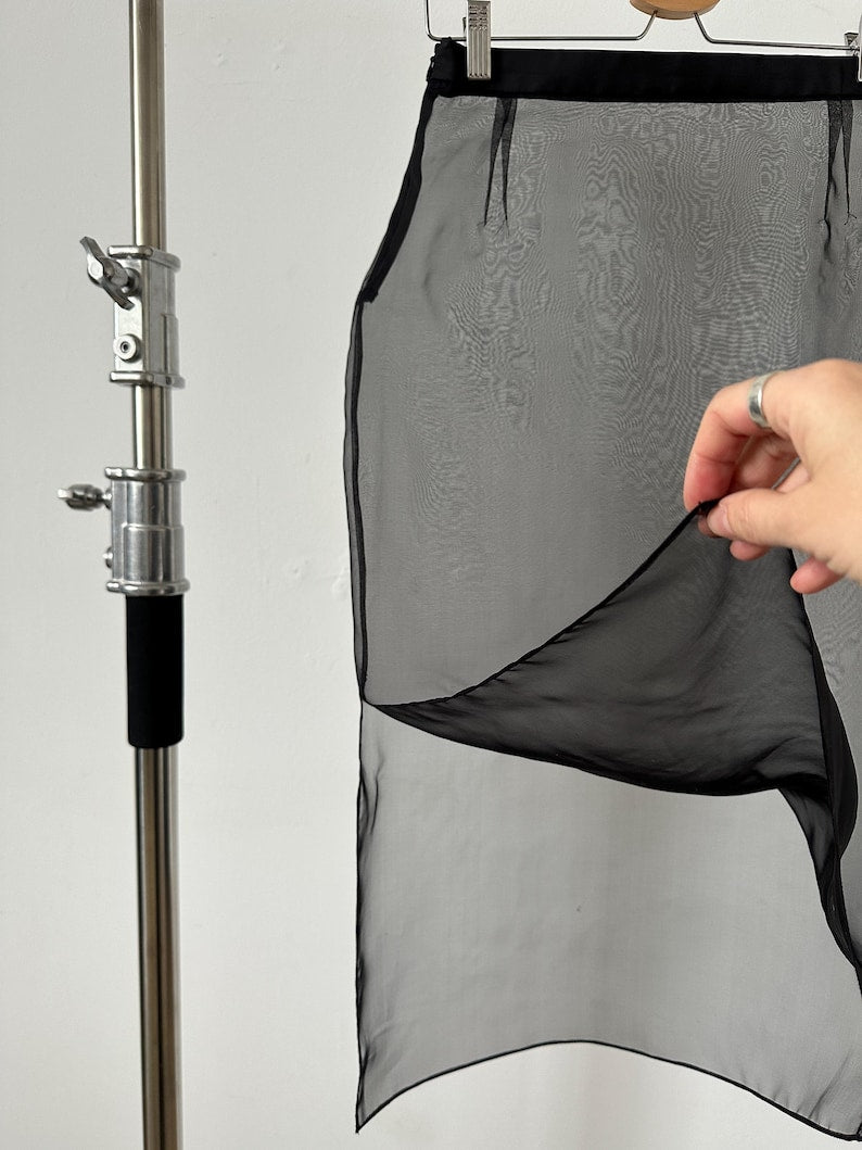 Black sheer skirt against a white wall and a hand showing the side slit of the skirt