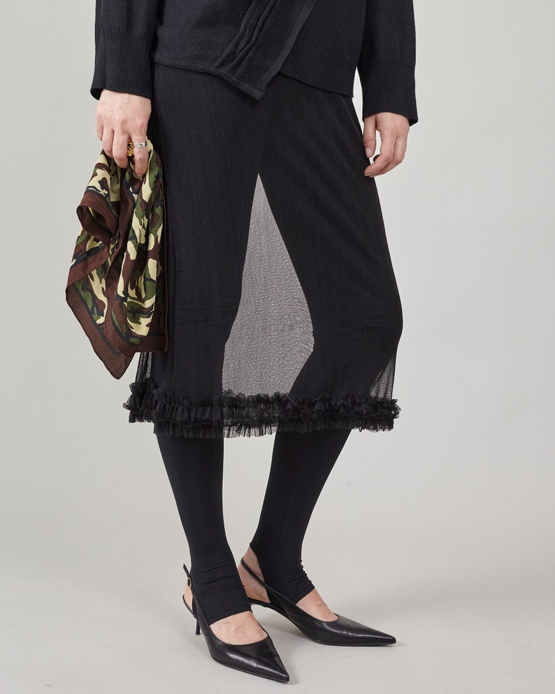 Person wearing a sheer ruffled skirt, midi cut, over black tights