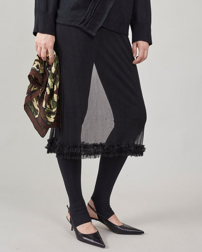 Person wearing a sheer ruffled skirt, midi cut, over black tights