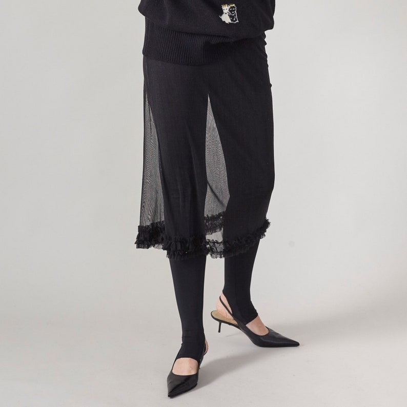 Black pants with sheer overlay and ruffled hem on a plain background
