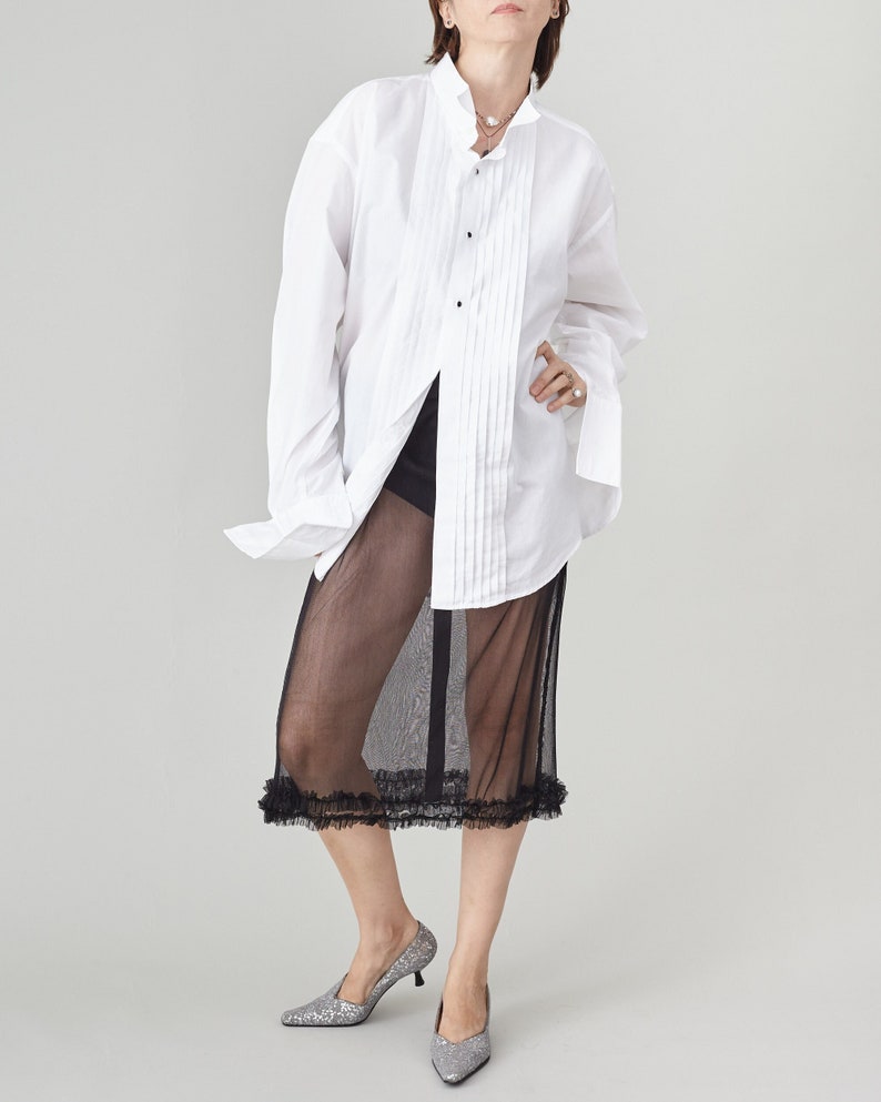 Person wearing a white shirt and black sheer skirt on a plain background