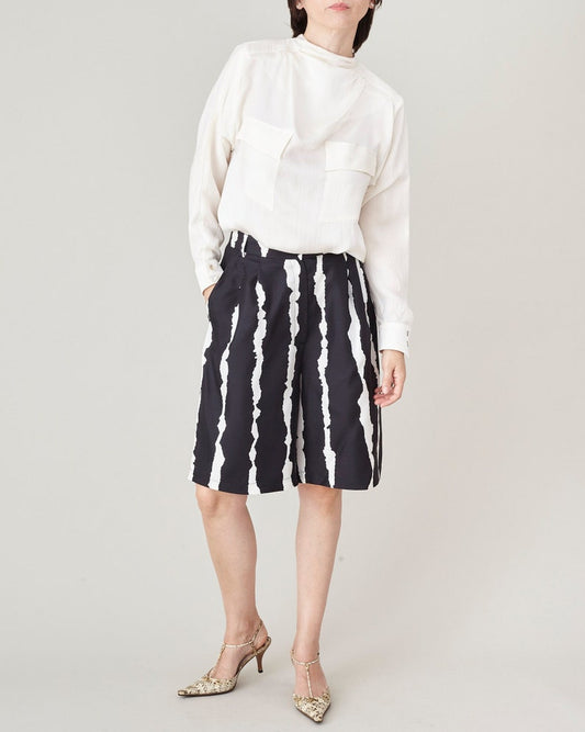 Front view of high-waisted silk Bermuda shorts in a black and white abstract print, styled with a white blouse.