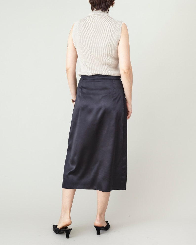 Person wearing a black satin skirt and beige top on a plain background