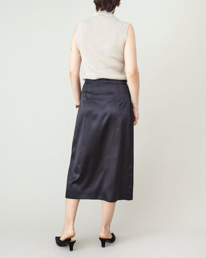 Person wearing a black satin skirt and beige top on a plain background