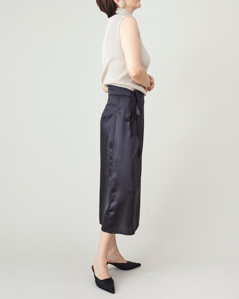 Person wearing a white sleeveless top and black satin silk skirt in studio