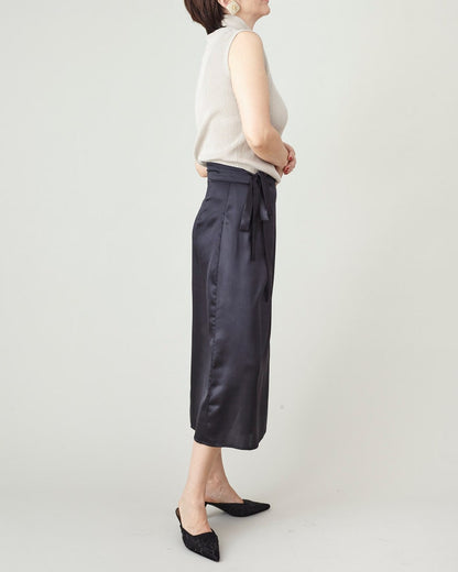 Person wearing a white sleeveless top and black satin silk skirt in studio