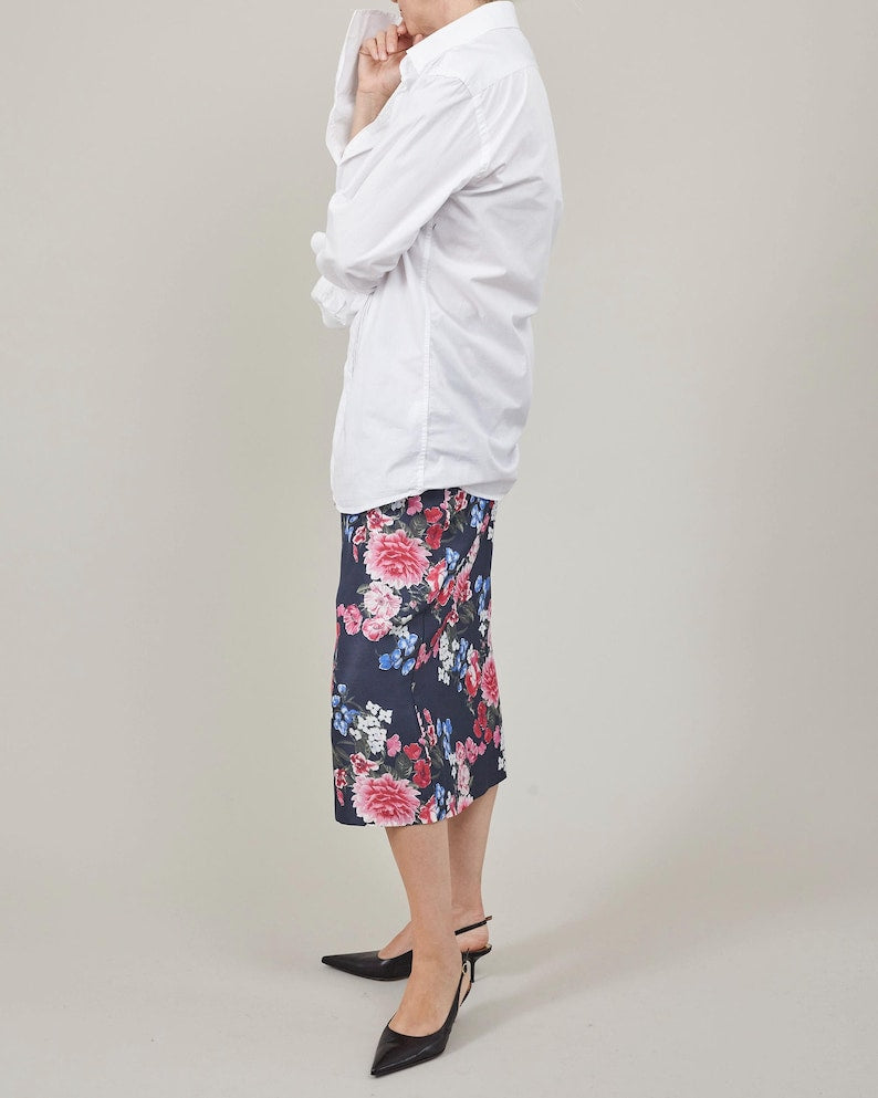 Person wearing a white top and floral skirt on a plain background