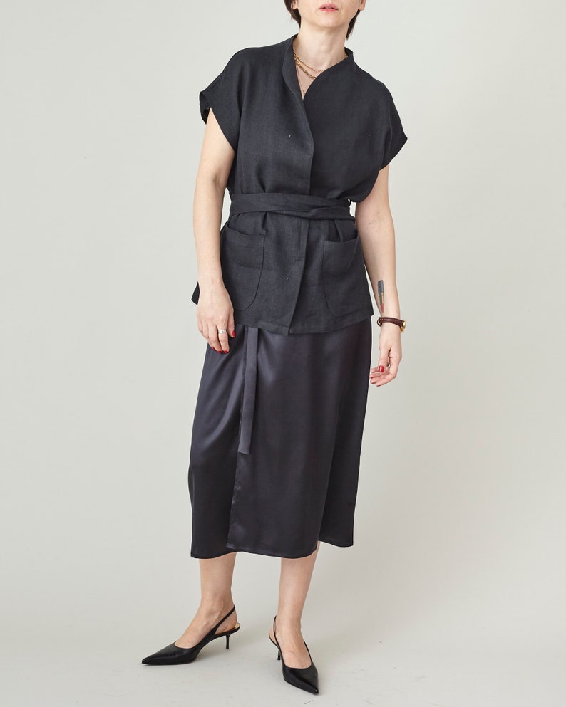 Person wearing a black outfit with a belt on a plain background