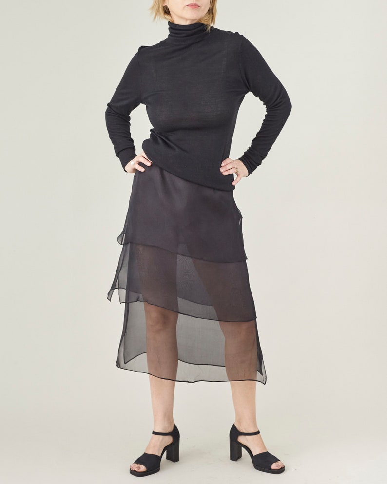 Person wearing a black long-sleeve top and sheer black skirt on a white background