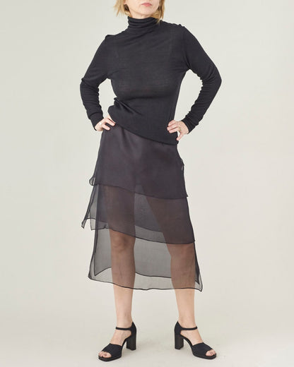 Person wearing a black long-sleeve top and sheer black skirt on a white background