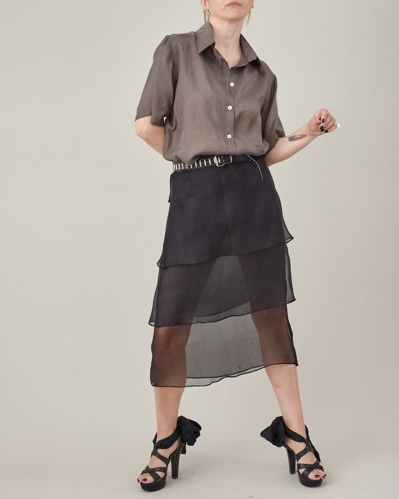 Person wearing a brown shirt and black layered skirt on a plain background