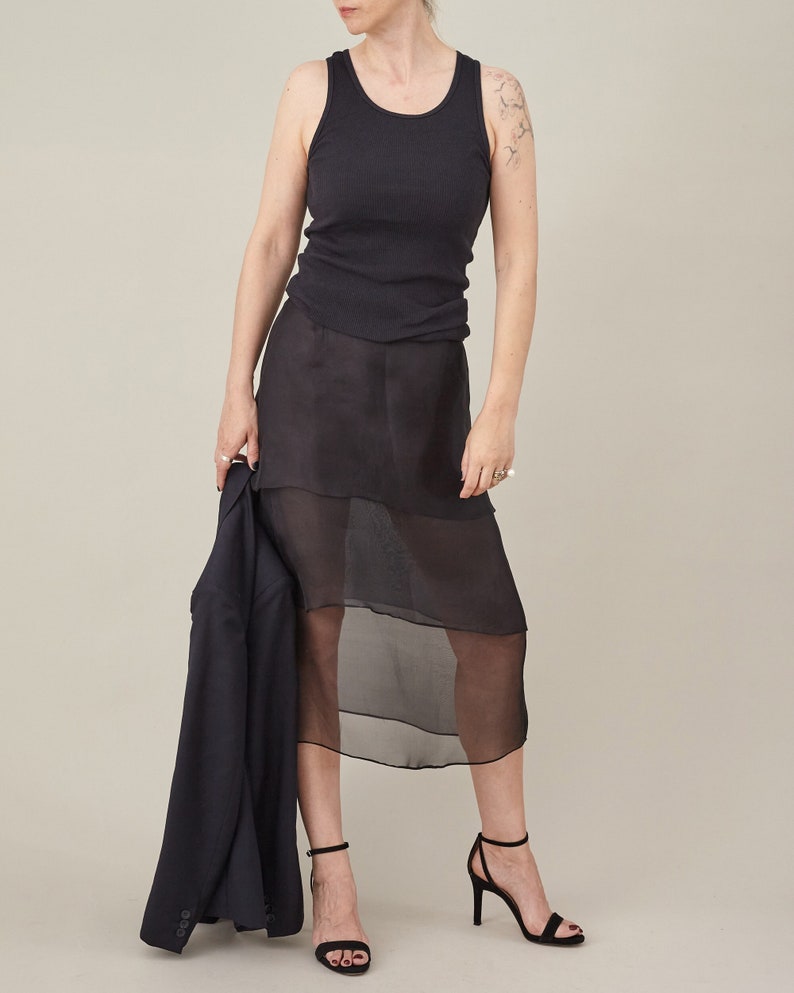 Woman wearing a black sleeveless top and sheer black skirt on a beige background