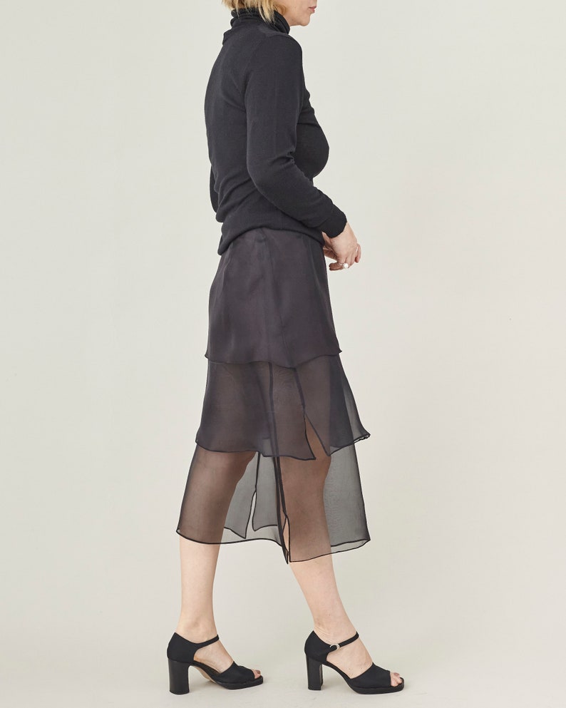 Person wearing a black top and sheer black skirt on a light gray background