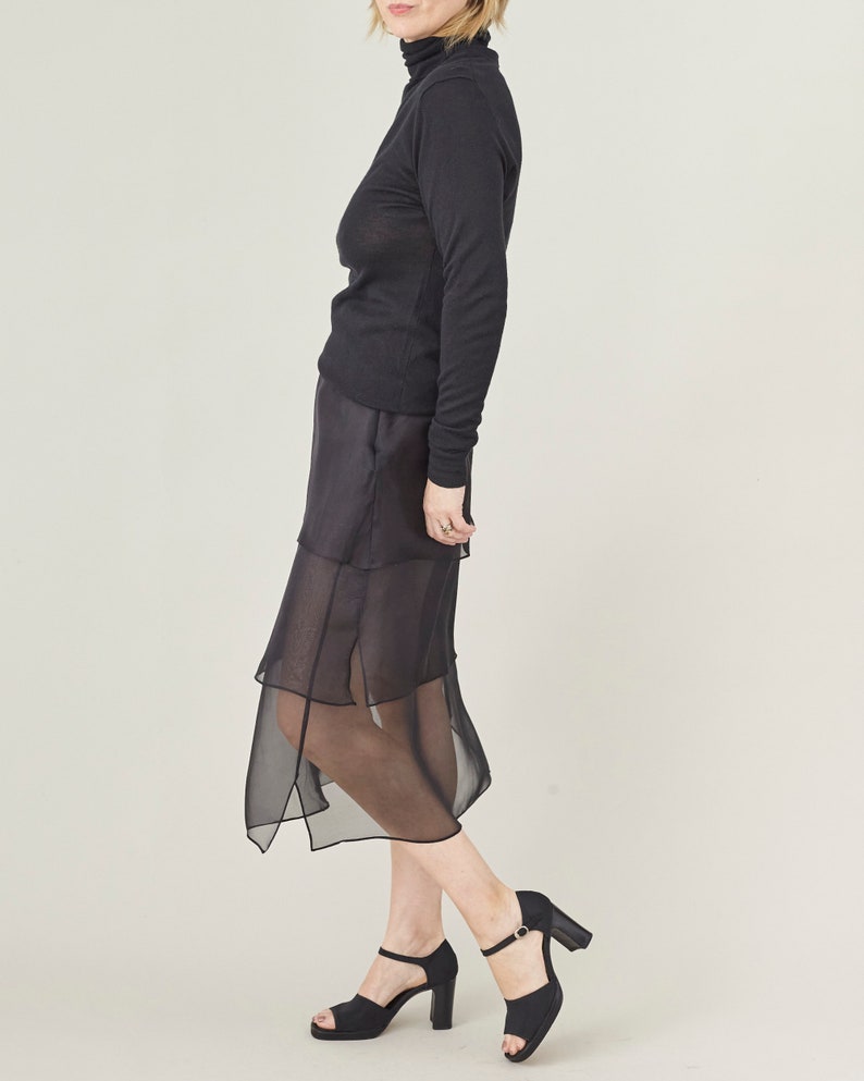 Person wearing a black turtleneck and sheer black skirt on a light gray background