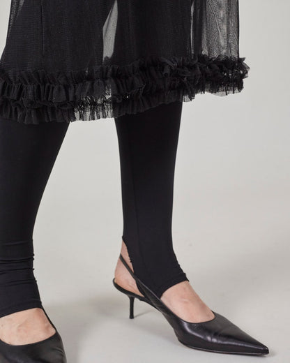 Black tights with ruffled hem skirt and black high-heeled shoes on a light gray background