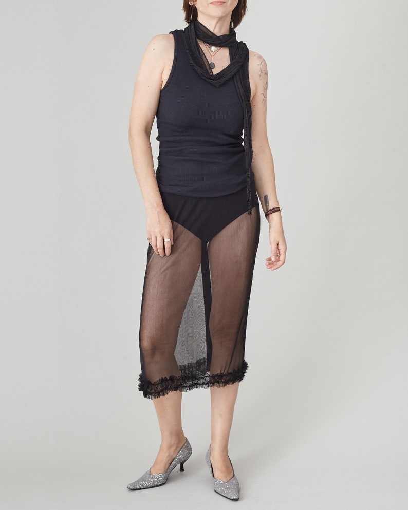 Person wearing a black sleeveless top and sheer black skirt on a gray background