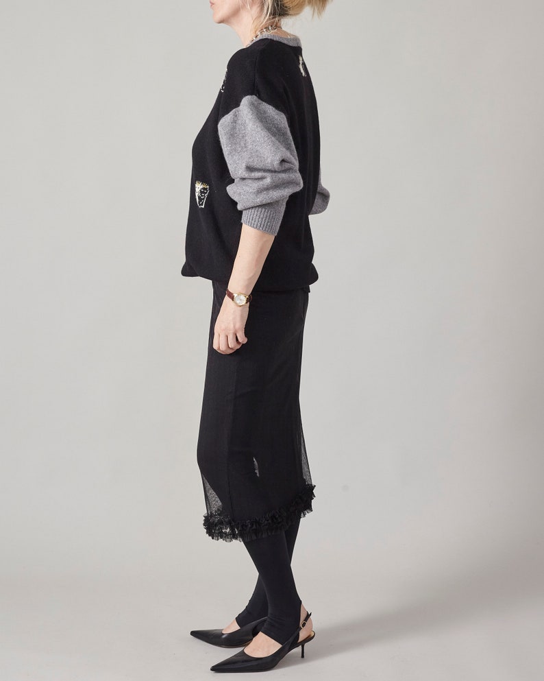 Person wearing a black outfit with a gray sweater on a plain background