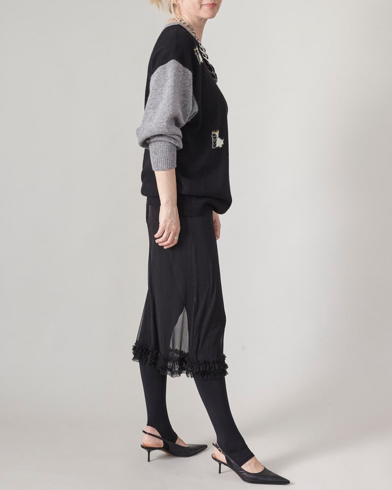 Person wearing a black outfit with a gray sleeve on a plain background