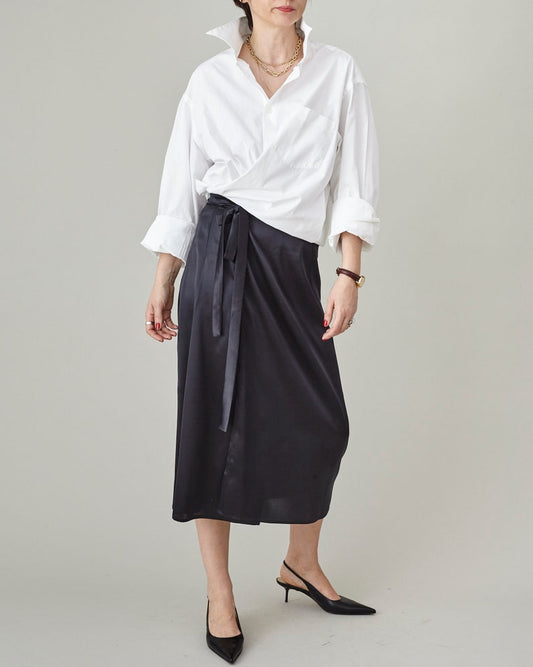 Person wearing a white shirt and black wrap, tie waist skirt oin a studio