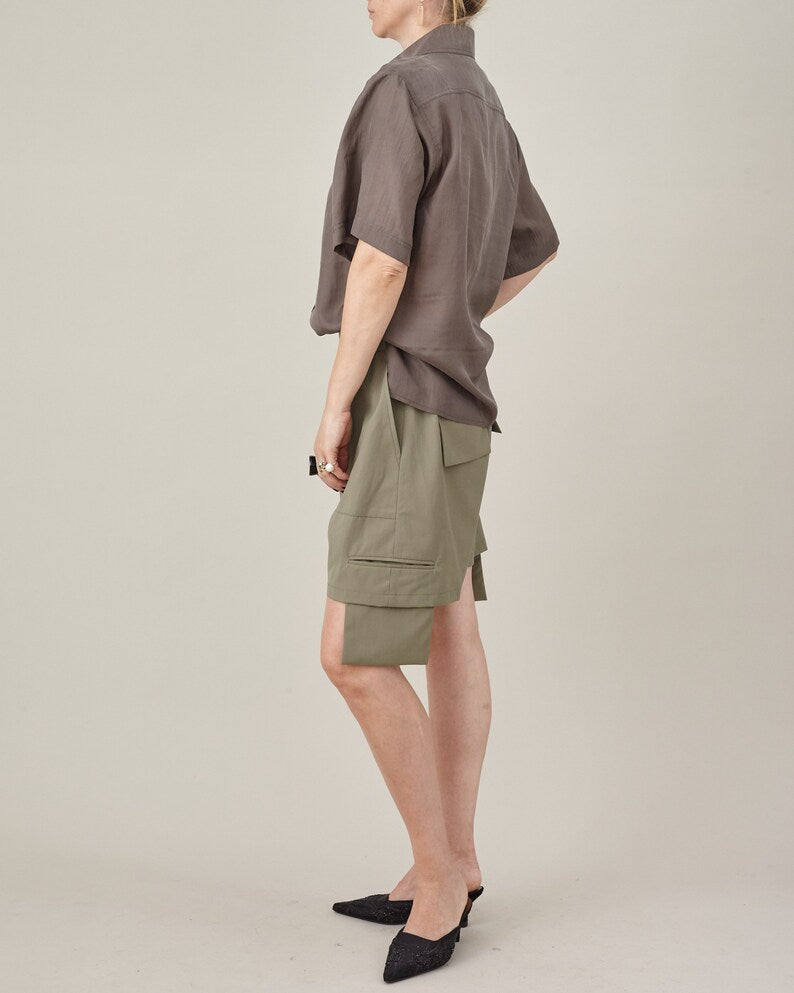 Back three-quarter view of the taupe silk short-sleeve blouse styled with khaki shorts.