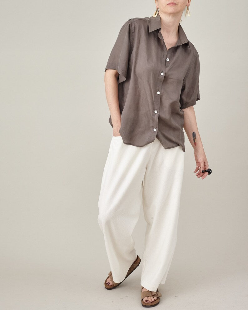 Taupe silk short-sleeve blouse worn loose with ivory pleated trousers.