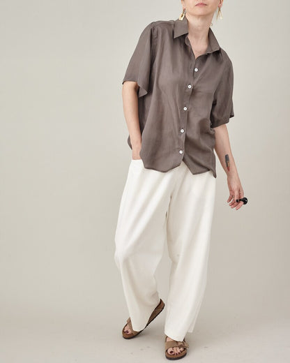 Taupe silk short-sleeve blouse worn loose with ivory pleated trousers.