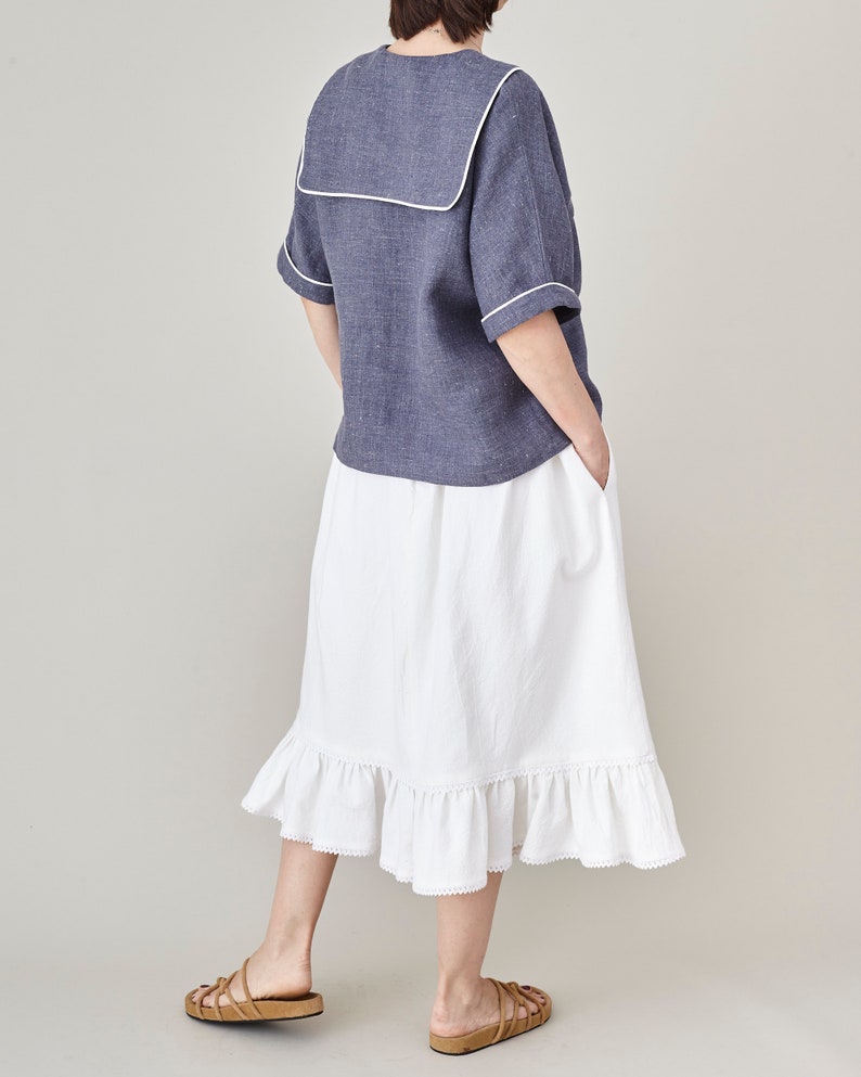 Person wearing a blue sailor top and white skirt on a plain background