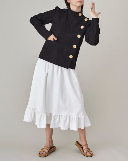 Person wearing a black jacket with wooden buttons and a white skirt on a plain background