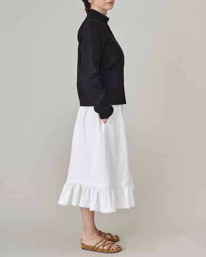 Person wearing a black top and white skirt with ruffled hem on a plain background