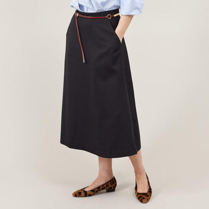 Person wearing a black skirt with a brown belt and animal print flats in a photo studio