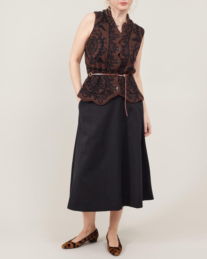Woman wearing a black sleeveless top with intricate brown patterns and a black A-line midi skirt on a white background