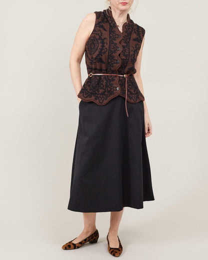 Woman wearing a black sleeveless top with intricate brown patterns and a black A-line midi skirt on a white background