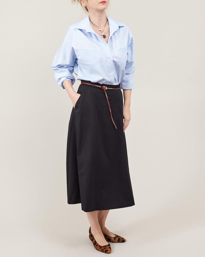 Person wearing a light blue shirt and black skirt with a belt on a plain background