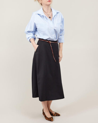 Person wearing a light blue shirt and black skirt with a belt on a plain background