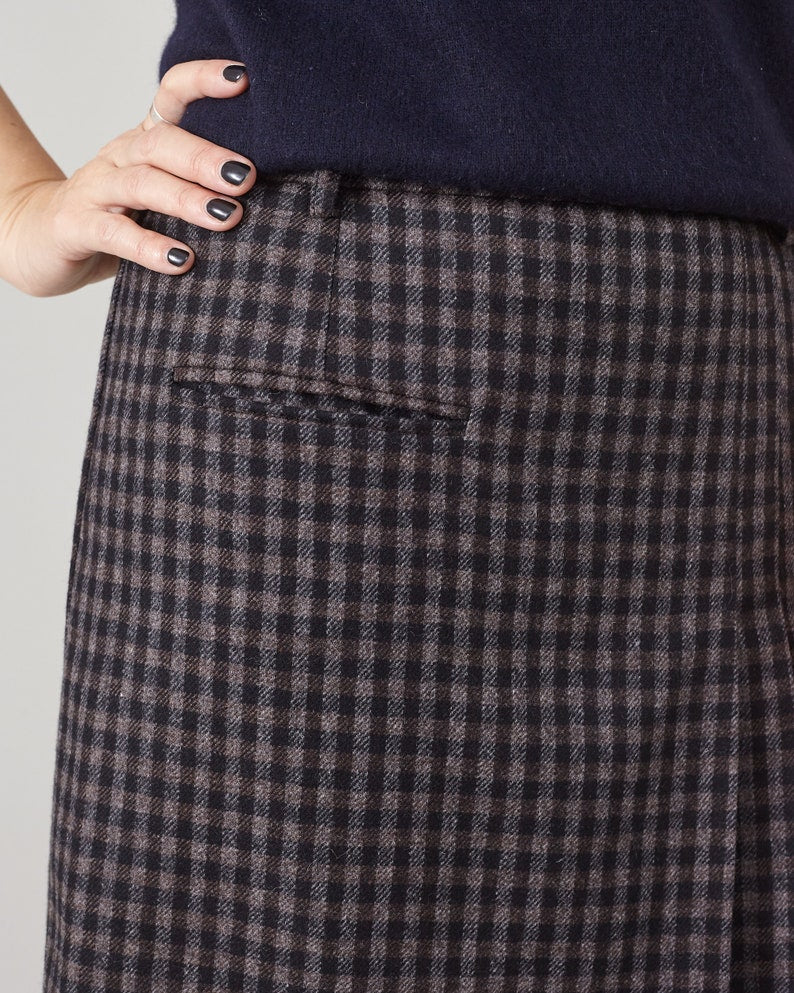 Close-up of a person wearing a dark blue sweater and brown checkered skirt on a light gray background